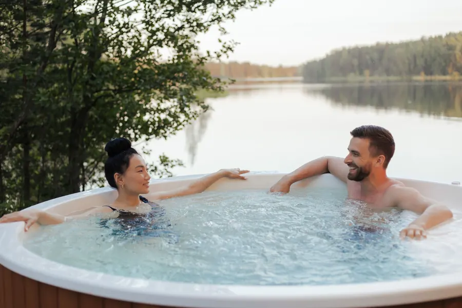 A couple relaxing in a hot tub by the water in the evening