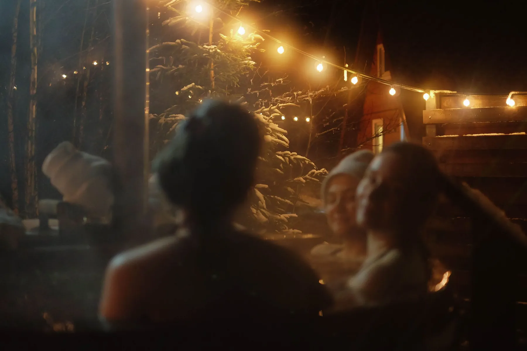 Friends in a steaming hot tub on a winter night under string lights