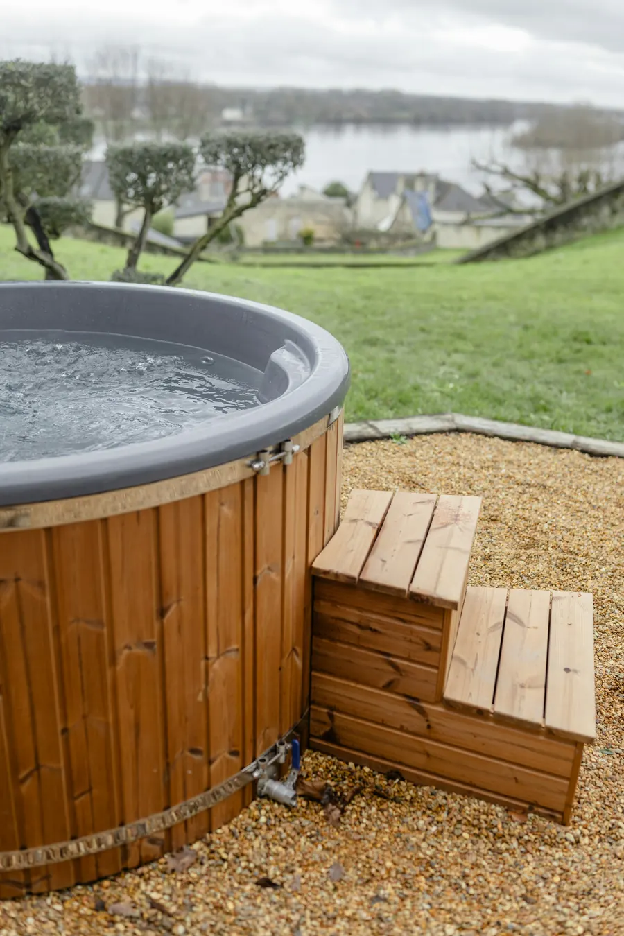 A modern hard-shell hot tub with wooden steps in a garden